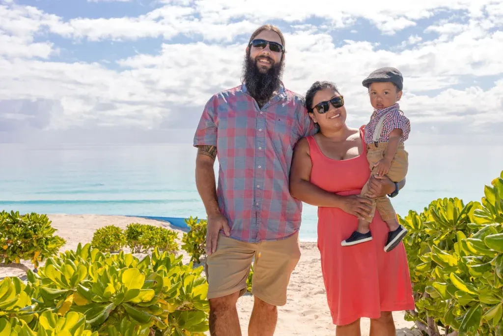 A young Canadian couple and their baby posing for a family photo session at Playa Delfines beach in Cancun, Mexico.